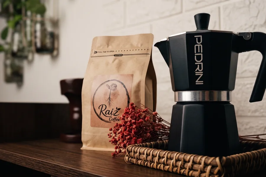 Cafetera italiana junto a una bolsa de café de Raíz sobre una bandeja de mimbre